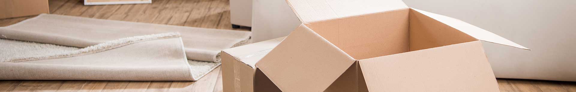 Boxes stacked in the living room of a new home with sunlight streaming through the windows.